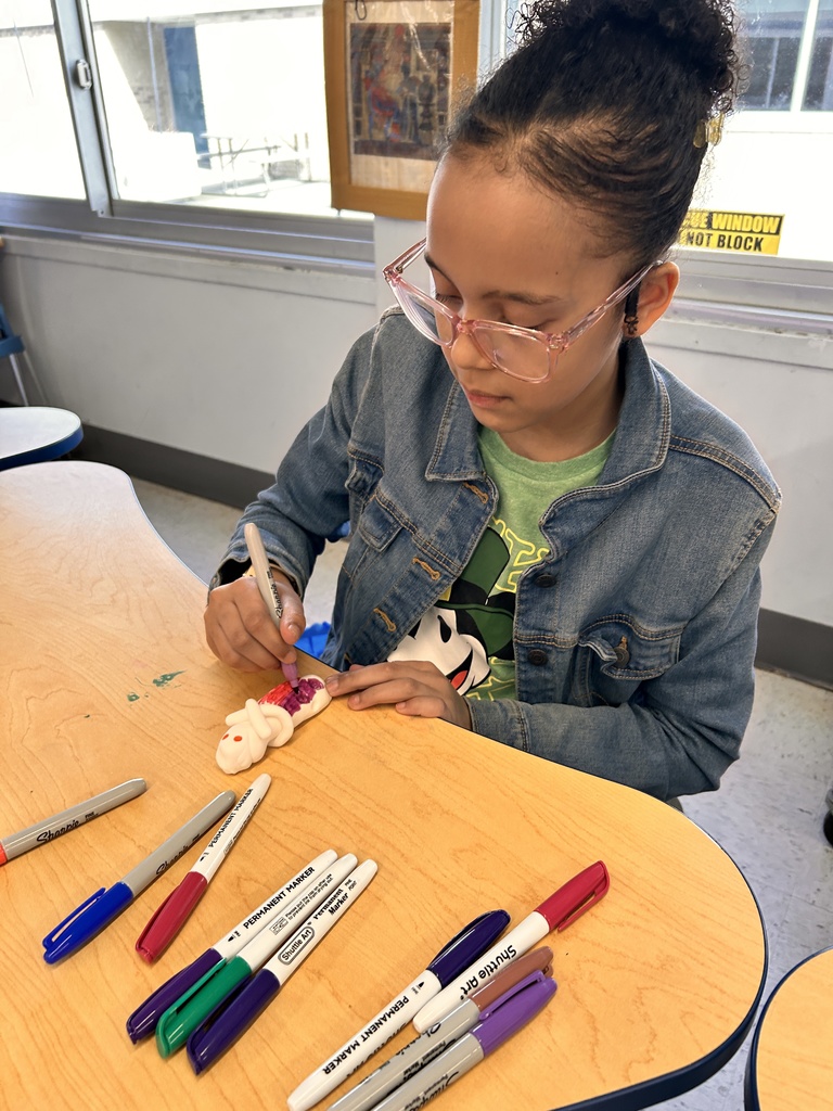 A student colors a Shabti with marker at a table.
