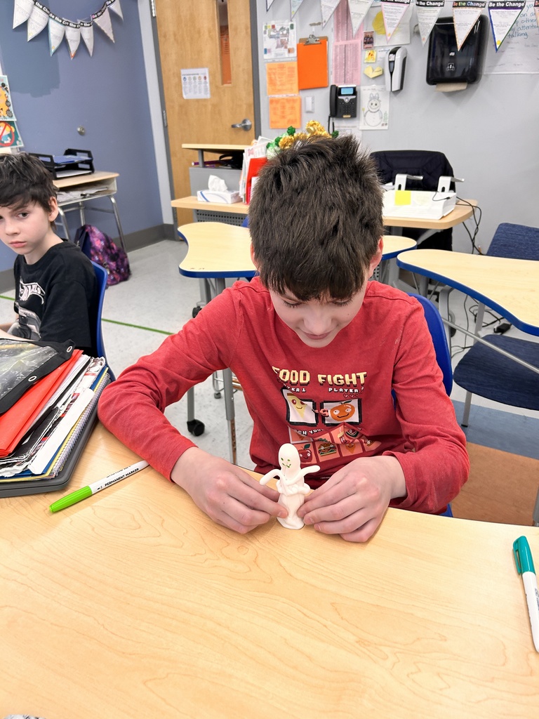 A student creates a Shabti out of clay at a table.