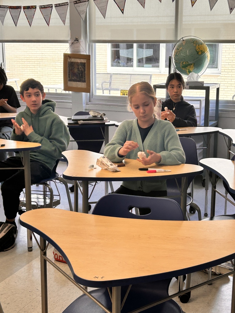 Students sitting at tables around a classroom create and color Shabtis.