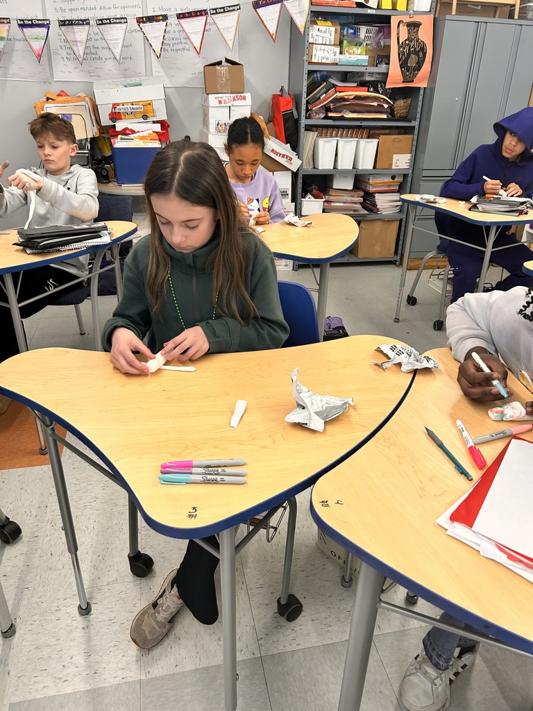 Students sitting at tables around a classroom create and color Shabtis.