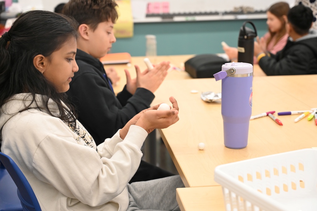 Students sitting at tables around a classroom create Shabtis out of clay.