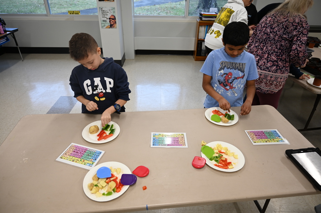 Two students cut vegetables on paper plates on a table to prepare for soup.