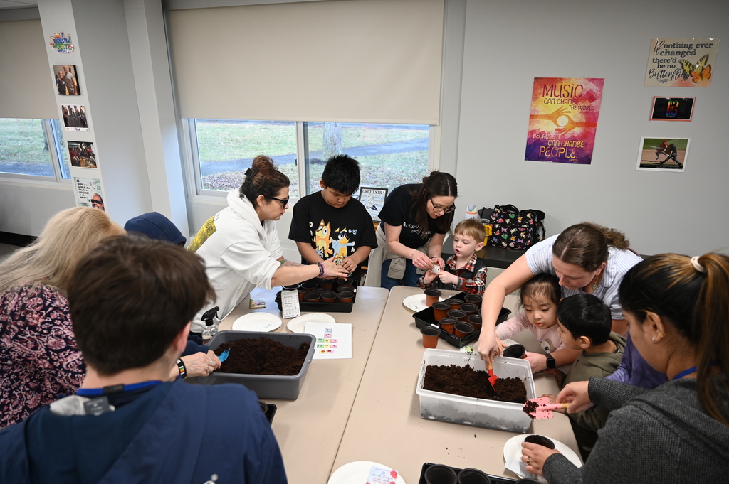Teachers help students dig for potatoes in plastic bins, using hand shovels.