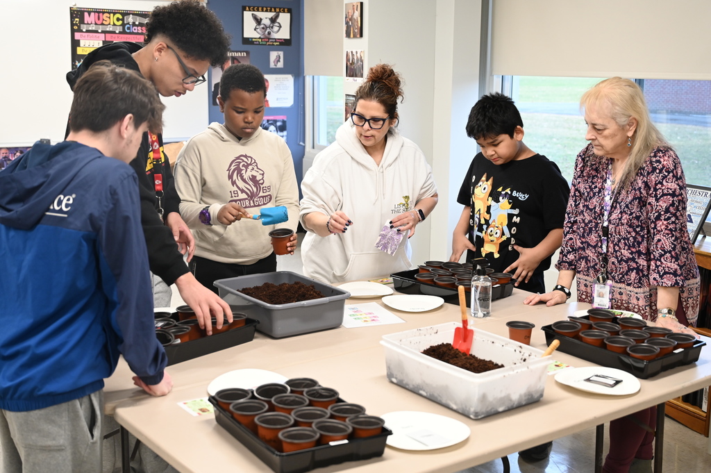 Teachers help students plant seeds in small cups.