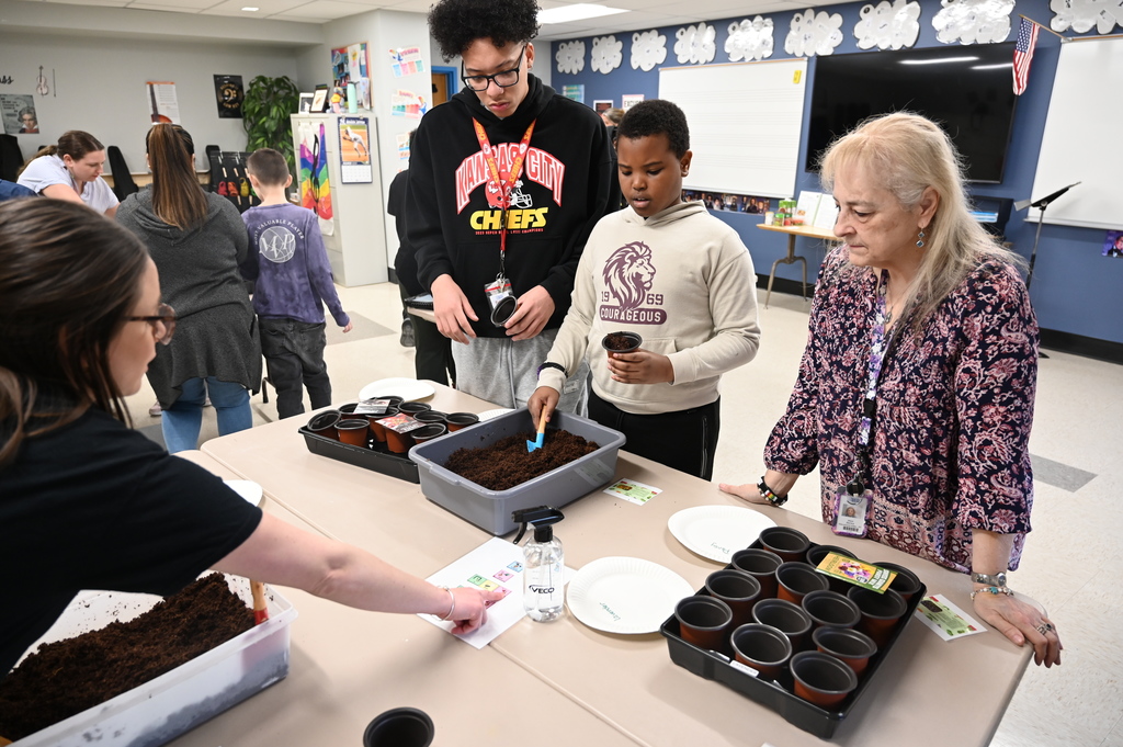 A student uses a hand shovel to put dirt into a cup.