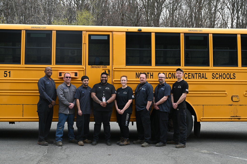 Eight North Colonie CSD mechanics stand together in front of a school bus.