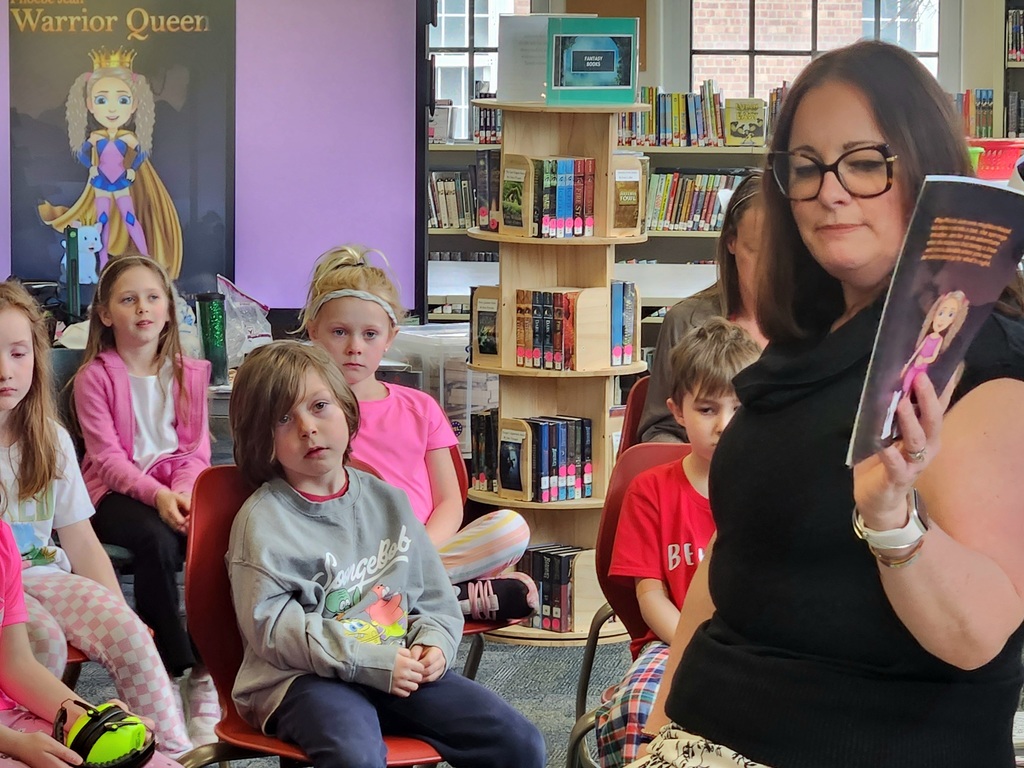 Mrs. Smith holds a book open as students look on.
