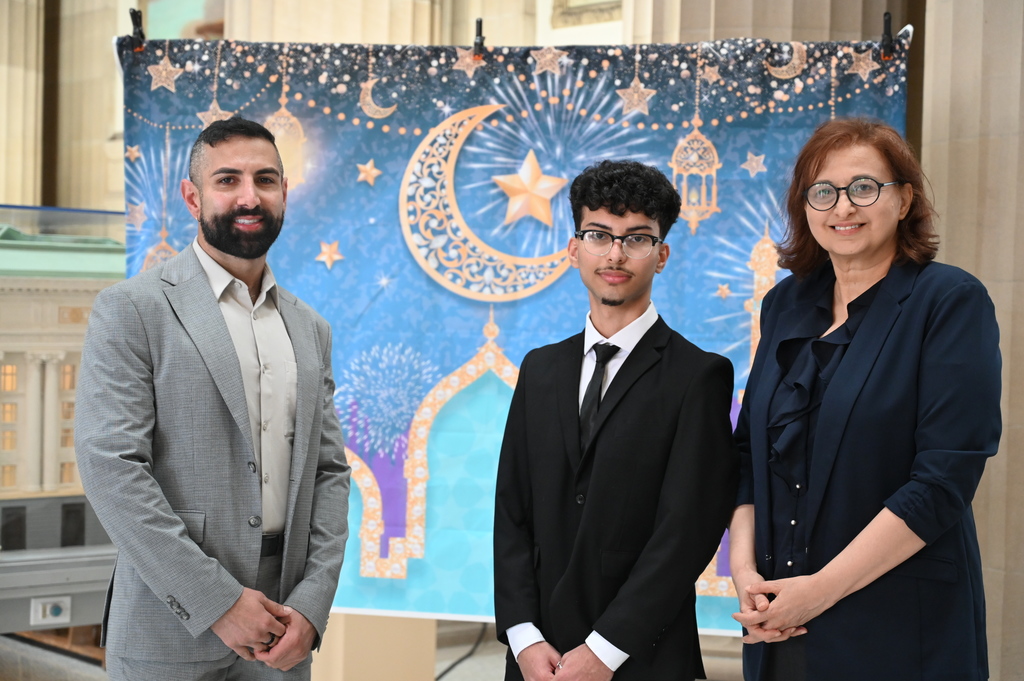Three people stand in front of a colorful backdrop at the Arab American Heritage Month celebration for NYSED.