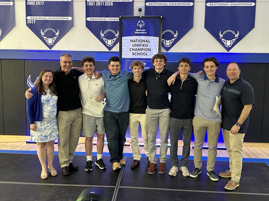 Unified coaches, athletes and partners pose together on stage in front of the banner.