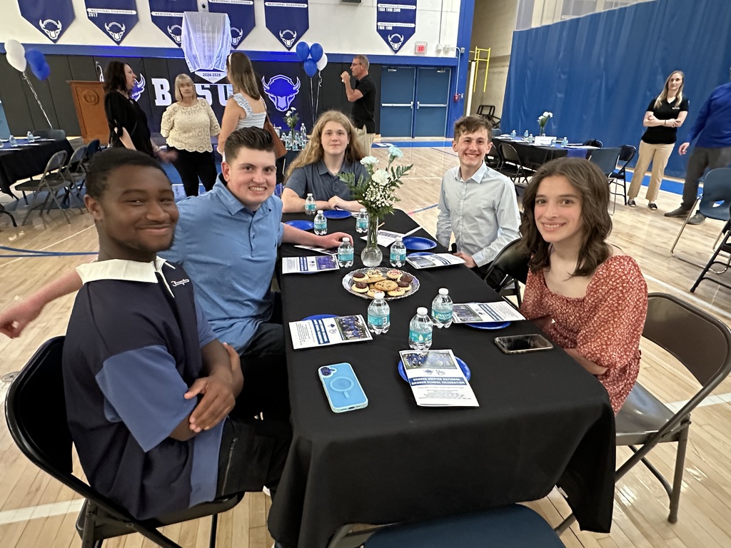 A group of students smile while seated at a table in the gymnasium.