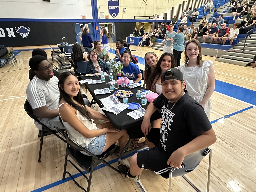 A group of students sit together around a table in the gymnasium.