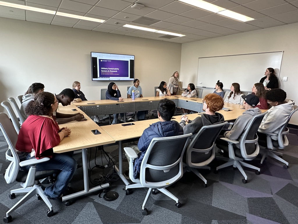 Students sit around a conference table and listen to two UAlbany professors speak about sustainability.