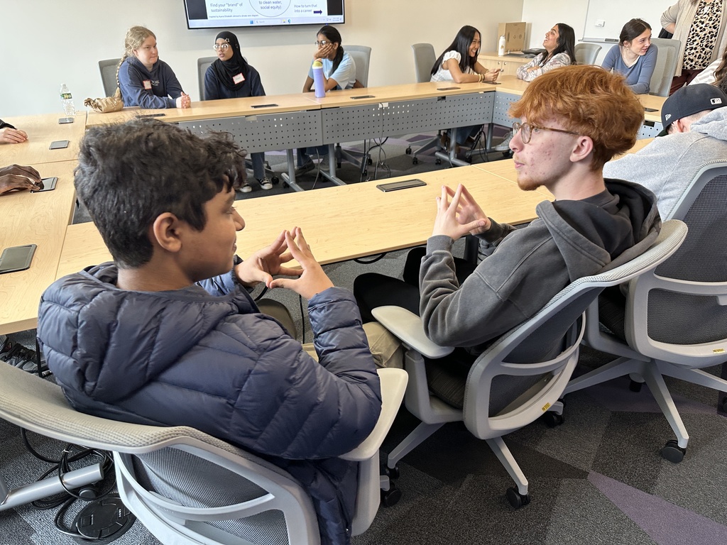 Two students discuss sustainability as a small group while seated at a conference table.