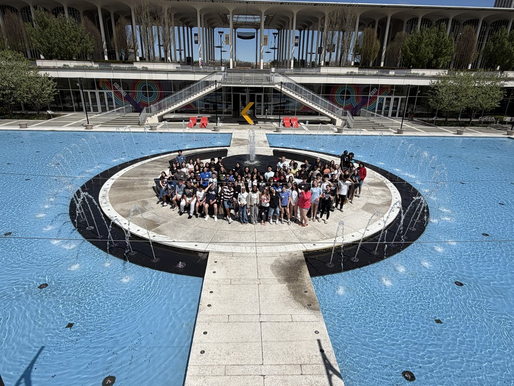 A wide photograph of a large group of Shaker freshmen posing around the UAlbany fountain.