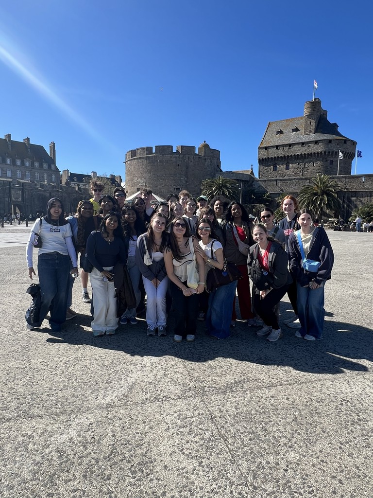 A large group of students pose in front of castle like buildings.