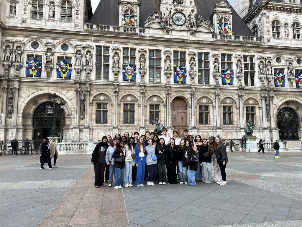 A large group of students pose in front of a beautiful building in France.