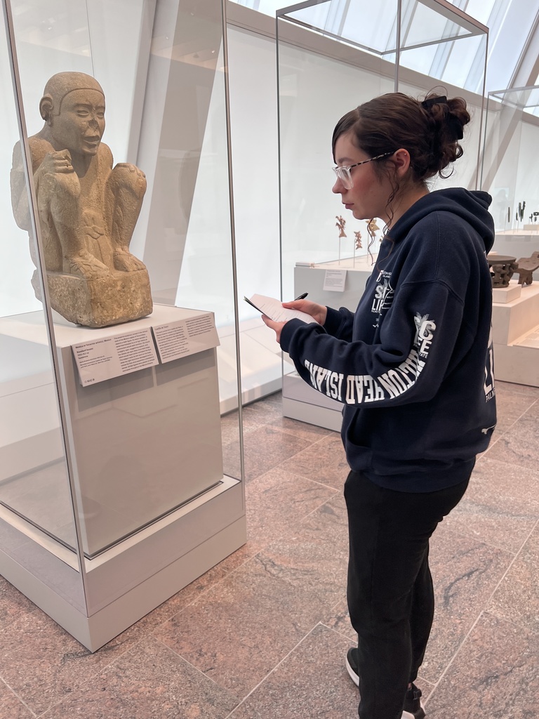 A student takes notes as she looks at an ancient artifact.