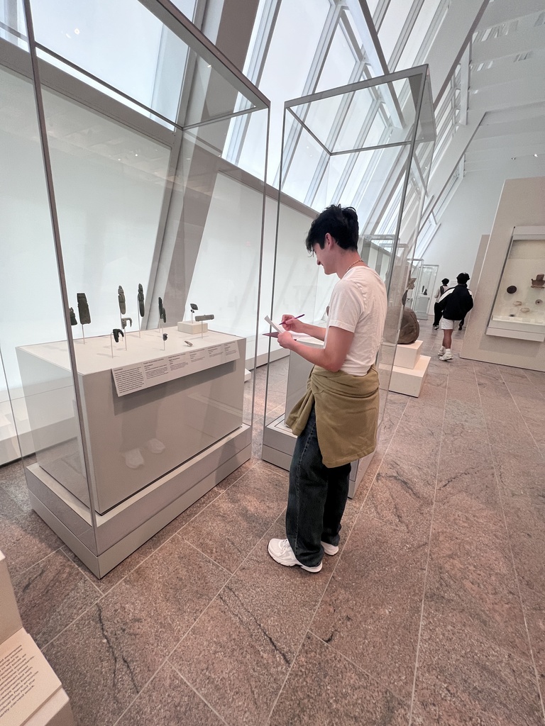 A student takes notes as he looks at ancient artifacts behind glass.