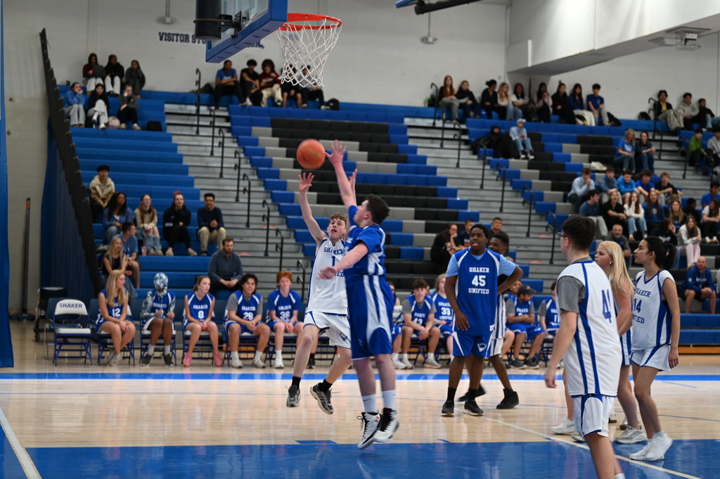 Blue team player tries to block white team player from making a basket