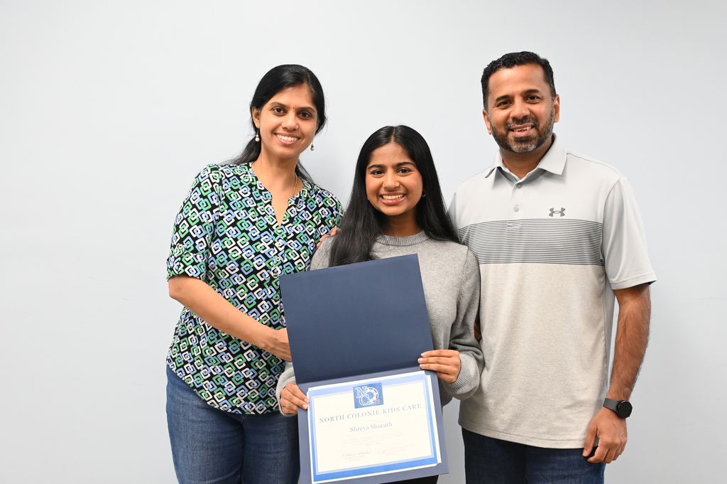 A student poses with her parents and a certificate of recognition.