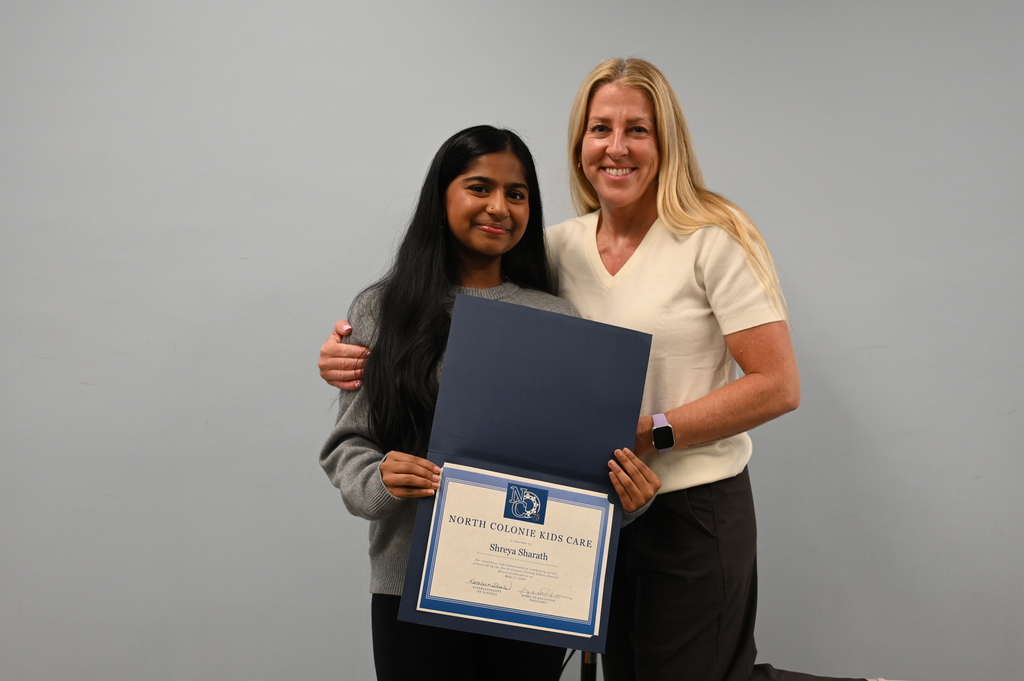 A student poses with her teacher and a certificate of recognition for Kids Care.