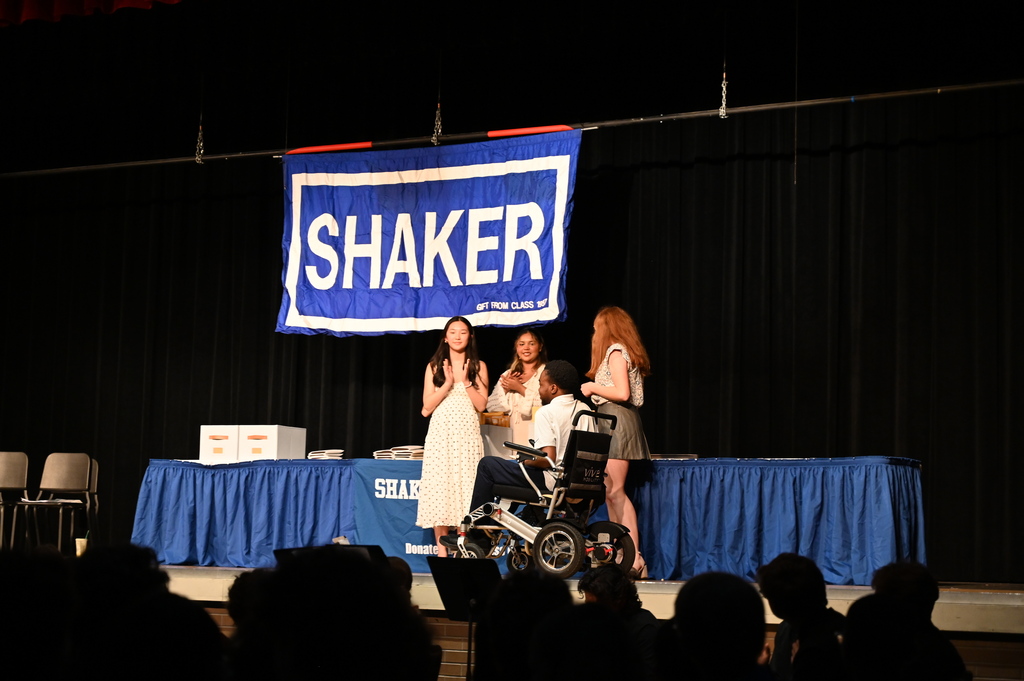 A student receives his award from other students who clap for him.