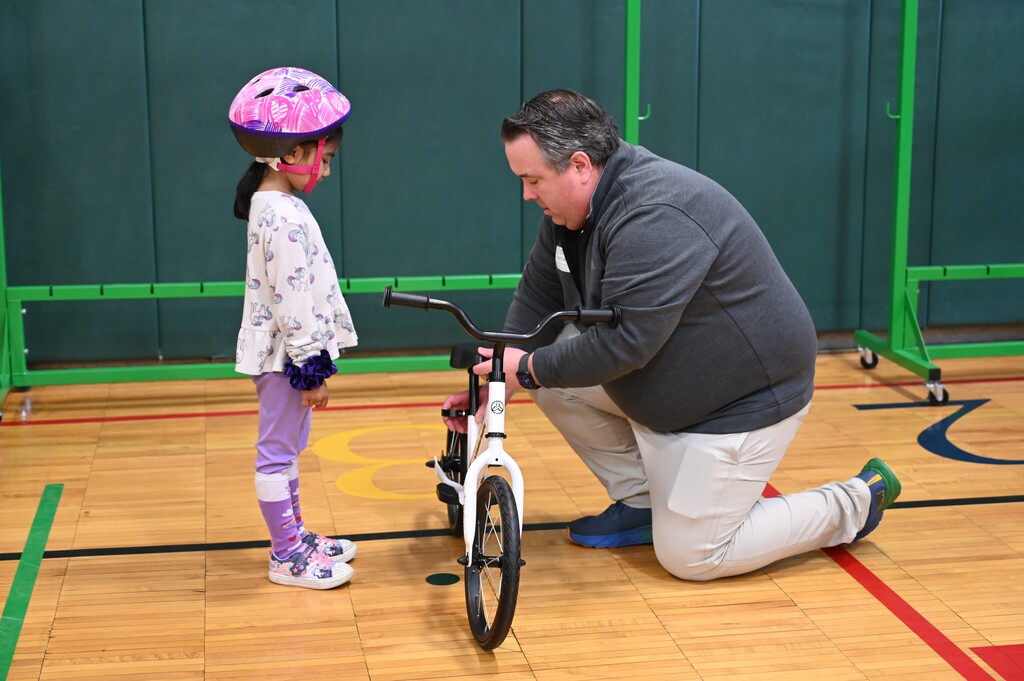 An instructor adjust the seat of a bike as a student in a helmet looks on.