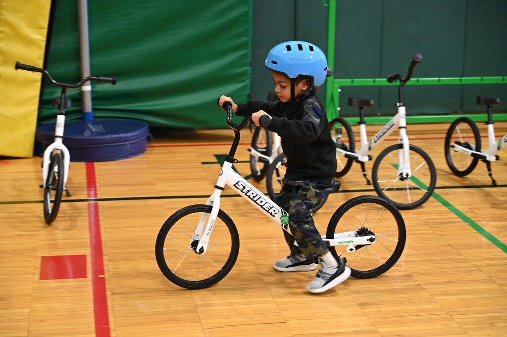 A young student rides a strider bike on the gym floor.