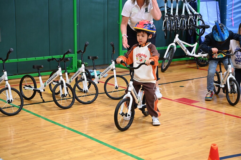 A young student rides a bike on the gym floor.