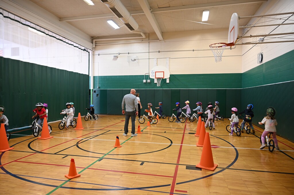 Students ride bicycles around traffic cones set up in the gymnasium.