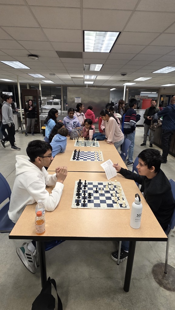 Students playing chess as adults look on.
