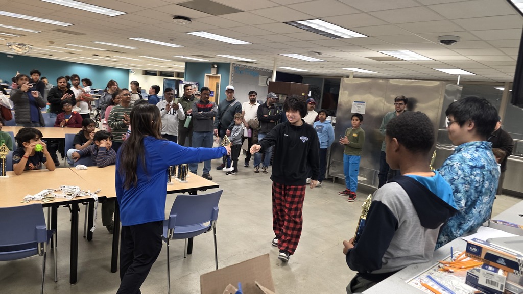 Two students go to shake hands after a chess match as others look on.