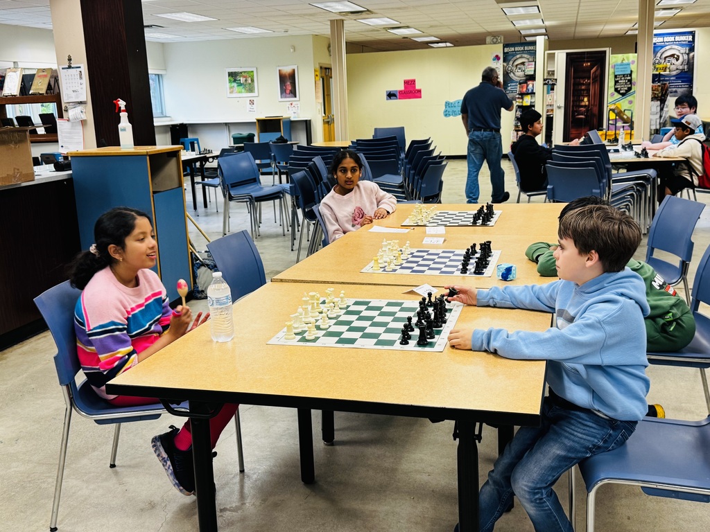 Students playing chess in a cafeteria at tables.