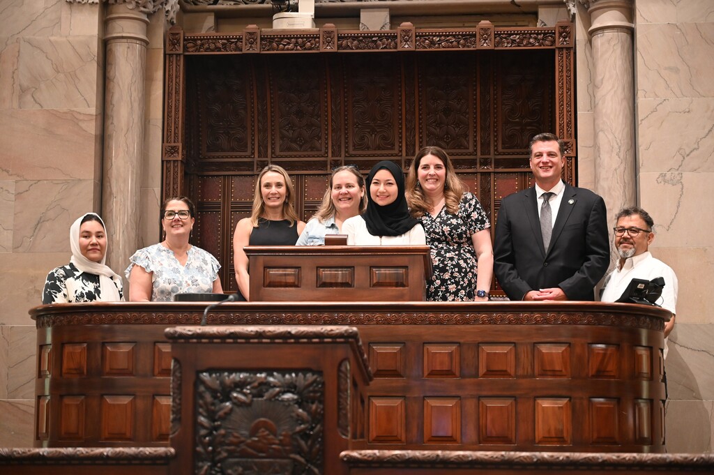 Sima poses at the Senate chamber dais with Senator Ashby and North Colonie teachers and administrators.