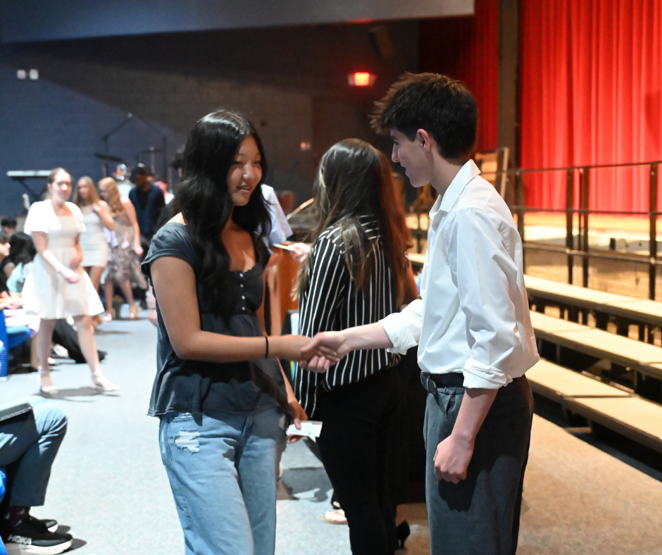 Student getting inducted into Tri-M Music Honor Society shaking hands with society officer