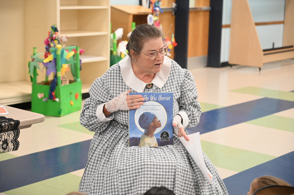 An actor sits in a chair and reads a book about Harriet Tubman.