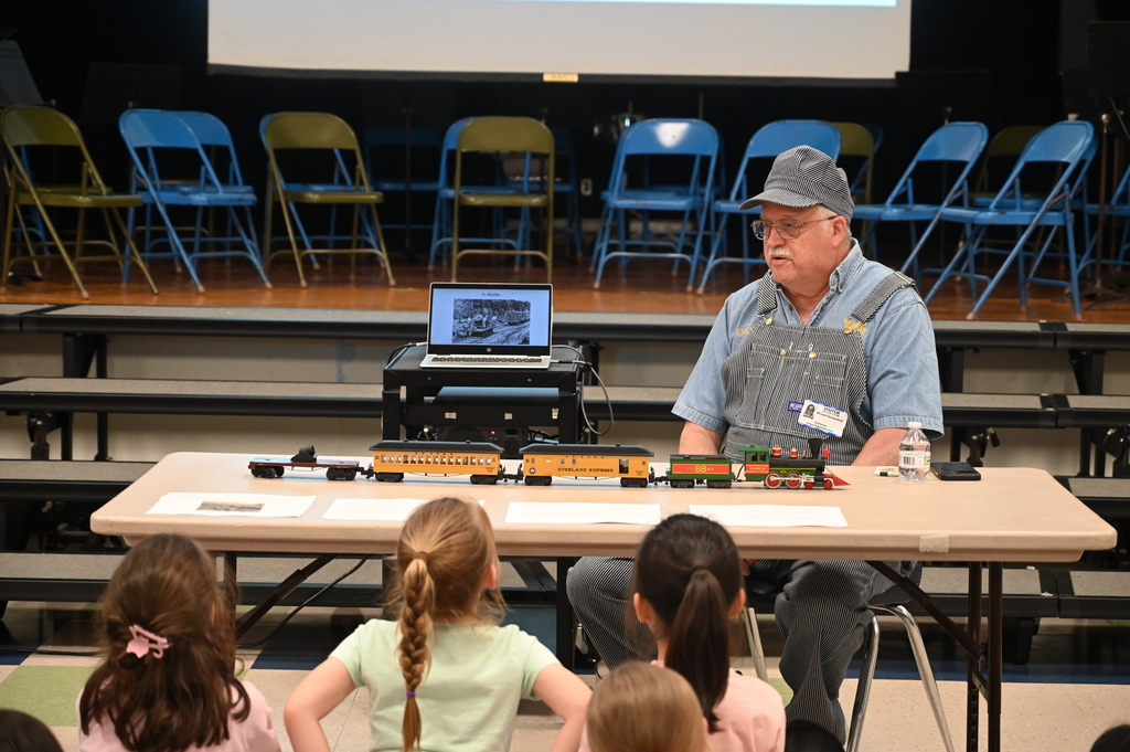 A reenactor dress in railroad clothing presents on the topic of railroads to students.
