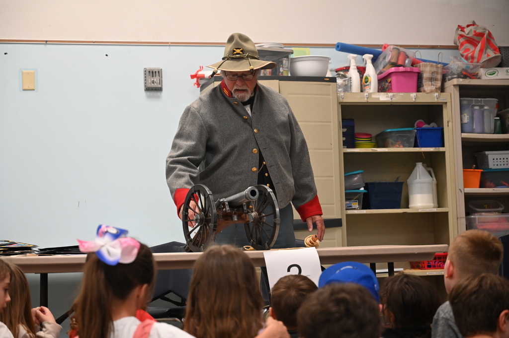 An actor portraying a soldier explains artillery to students seated in front of him.