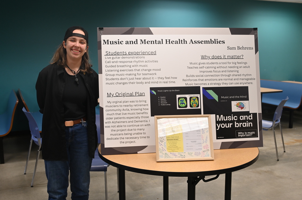 student posing with a sign stating music and mental health assemblies