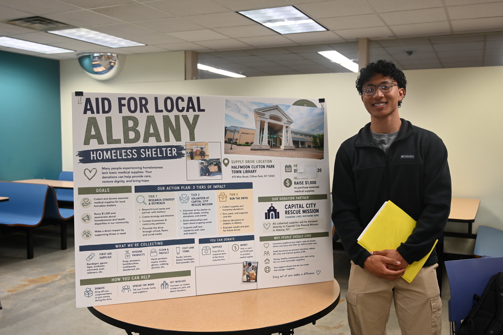 student posing with a sign stating aid for local albany homeless shelter