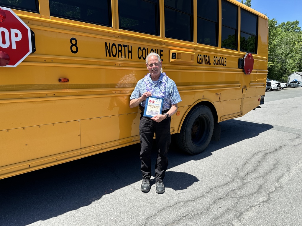 Bus driver, Mr. Stew, holds a plaque while standing in front of a school bus.