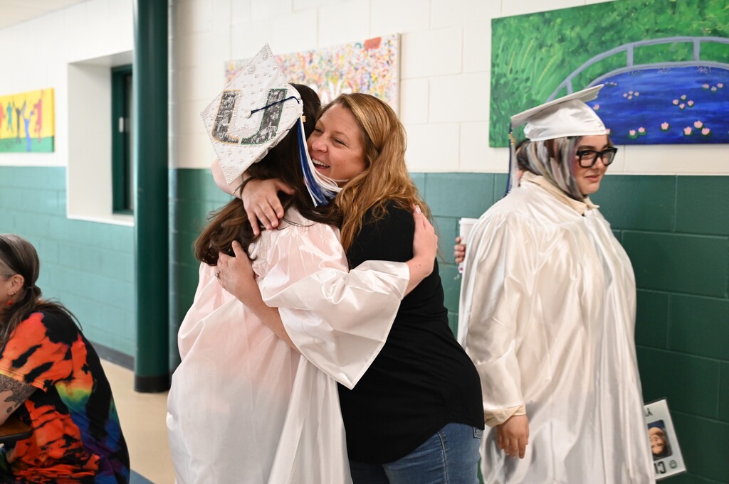 A teacher hugs one of her former students who is wearing a cap and gown.