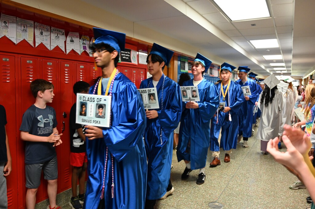 Graduating seniors walk down the hall lined with elementary students and teachers.