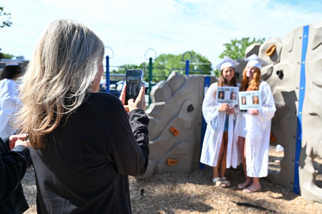 An adult takes a photo on her phone of two graduating seniors.
