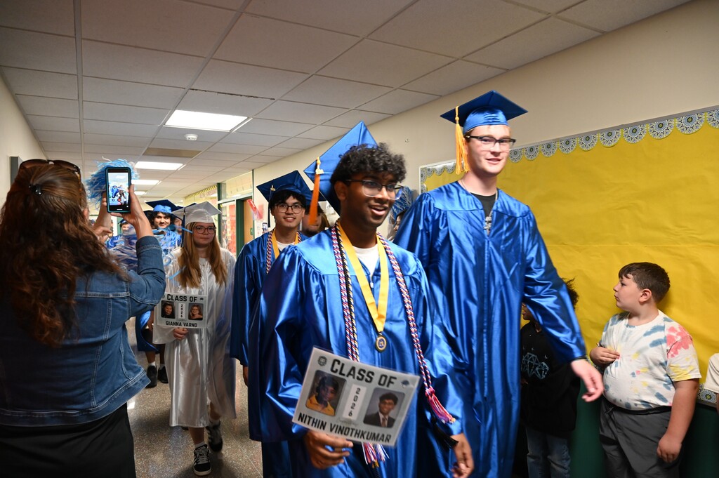 Graduating seniors walk through the halls as elementary students and teachers look on.