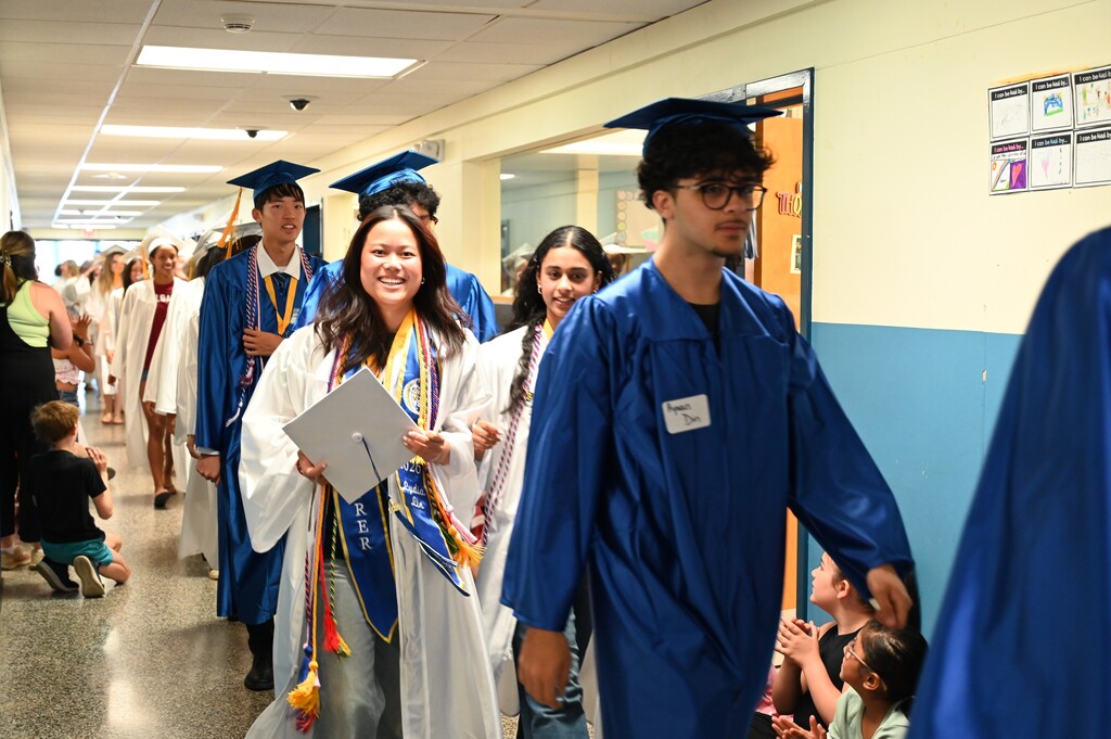 Graduating seniors in cap and gown walk through the halls of their elementary school.