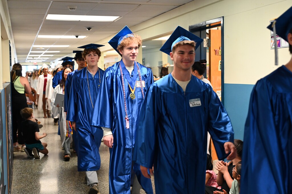 Graduating seniors walk down the hallways of their former school in their caps and gowns.