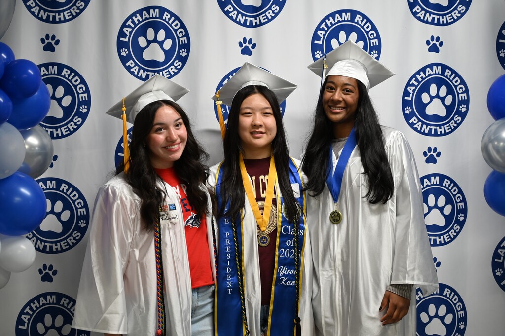 Three graduating seniors pose together in caps and gowns.