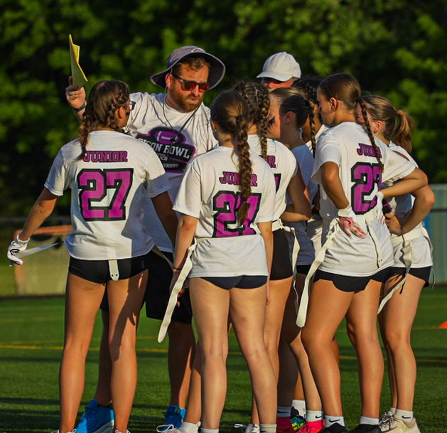 A coach reads the plays to a huddle of junior players.