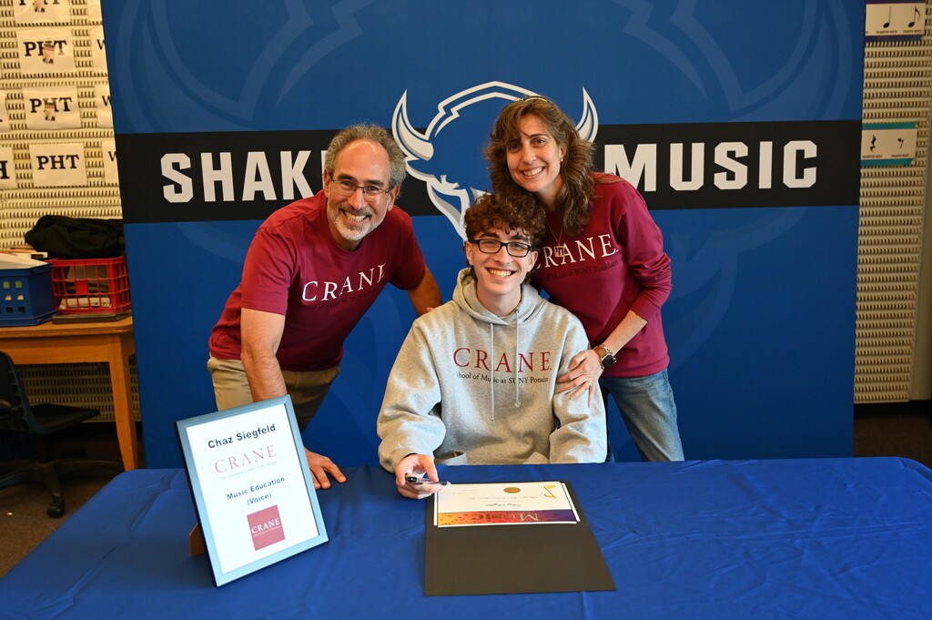 A student poses at a table with their family after signing.